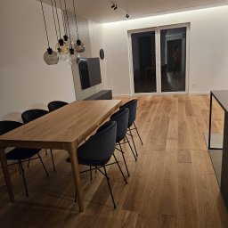 Tomasz Skoczylas - Nowoczesna jadalnia z drewnianym stołem, krzesłami na metalowych nogach i parkietem. Nad stołem designerska lampa z kilkoma szklanymi kloszami. Minimalistyczny wystrój.