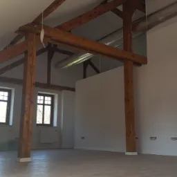 Przestronne, odnowione poddasze z drewnianą konstrukcją nośną, świeżo pomalowanymi ścianami i nową podłogą z widocznymi puszkami elektrycznymi.