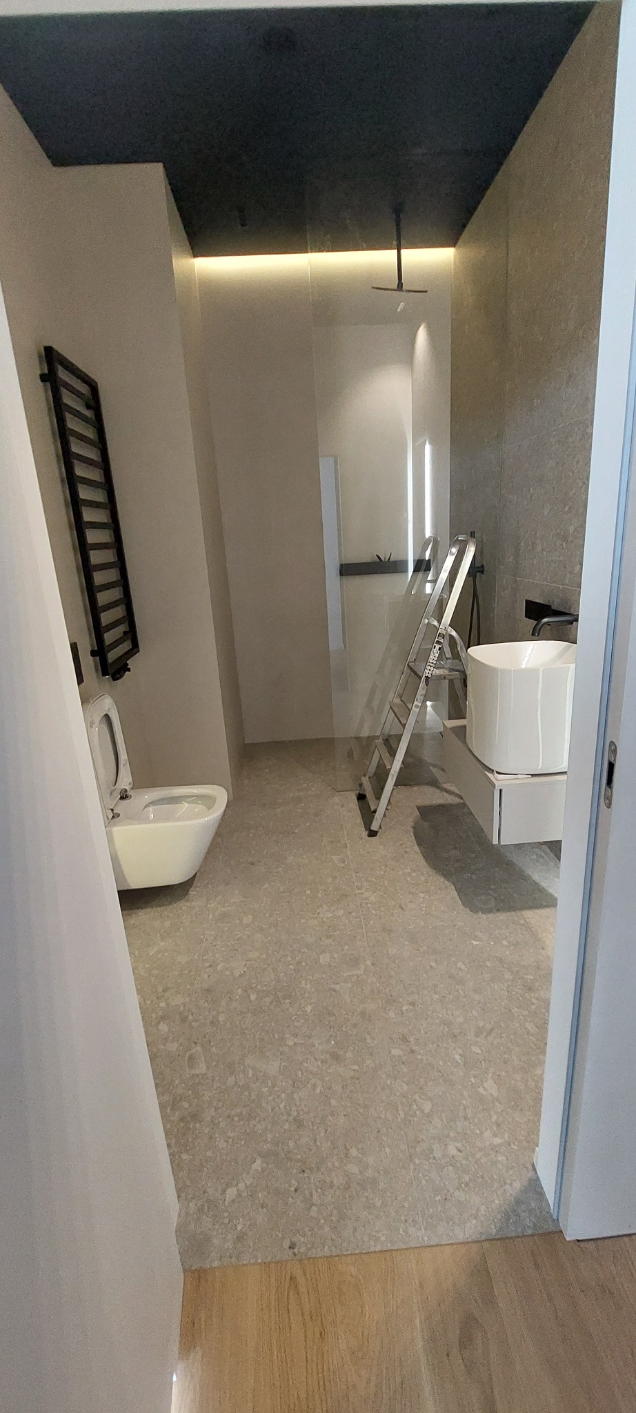 Nowoczesna łazienka w trakcie wykańczania: biała ceramika, drabinka grzewcza, szara glazura i drabina malarska. Minimalistyczny design z oświetleniem LED.