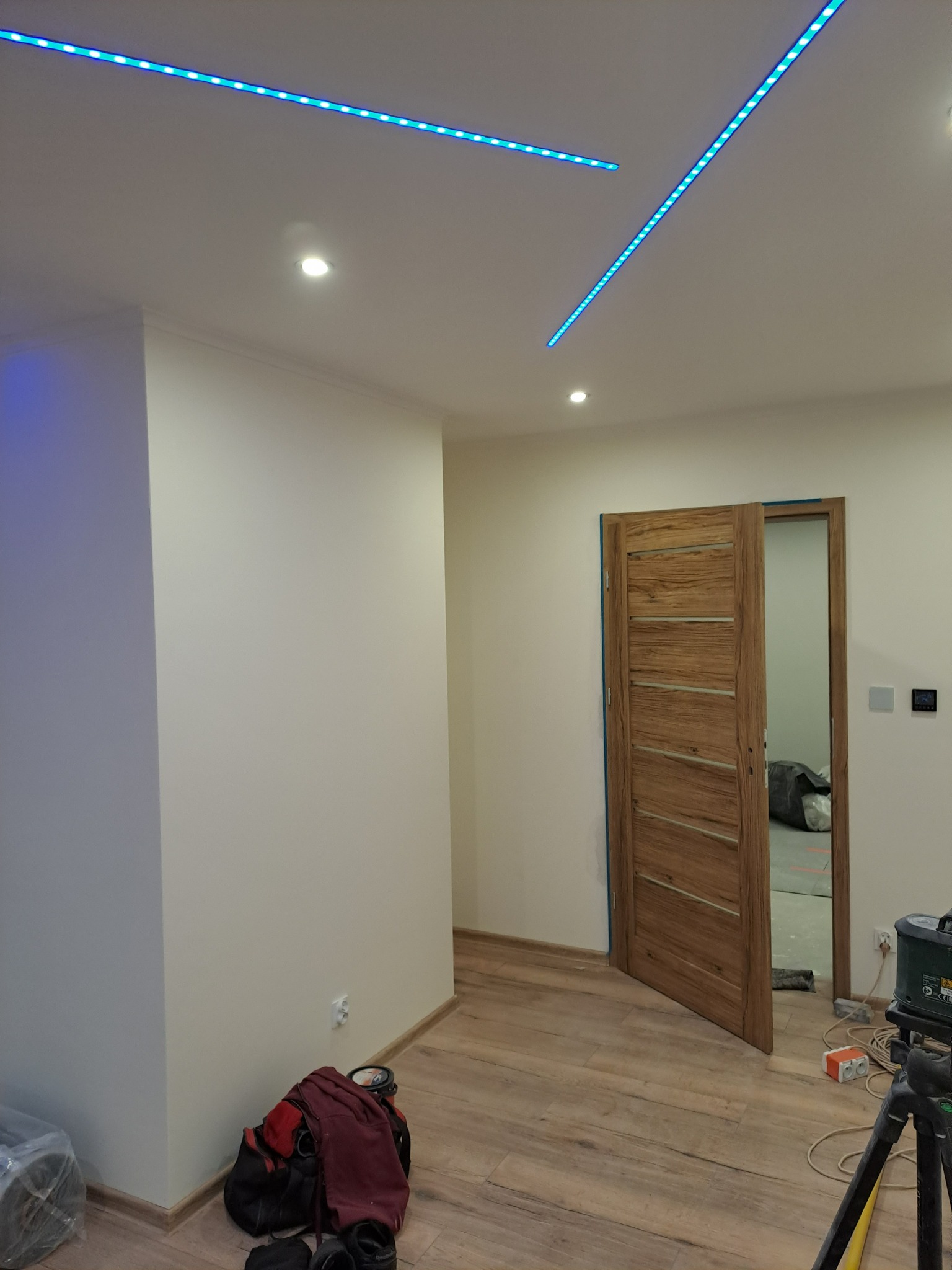 Wnętrze pokoju z drewnianą podłogą, otwartymi drewnianymi drzwiami i dekoracyjnym oświetleniem LED na suficie.