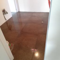 Marek Francewicz - Świeżo ułożone, brązowe płytki podłogowe z plastikowymi krzyżykami dystansowymi w jasnym pomieszczeniu, widok zza białych drzwi.