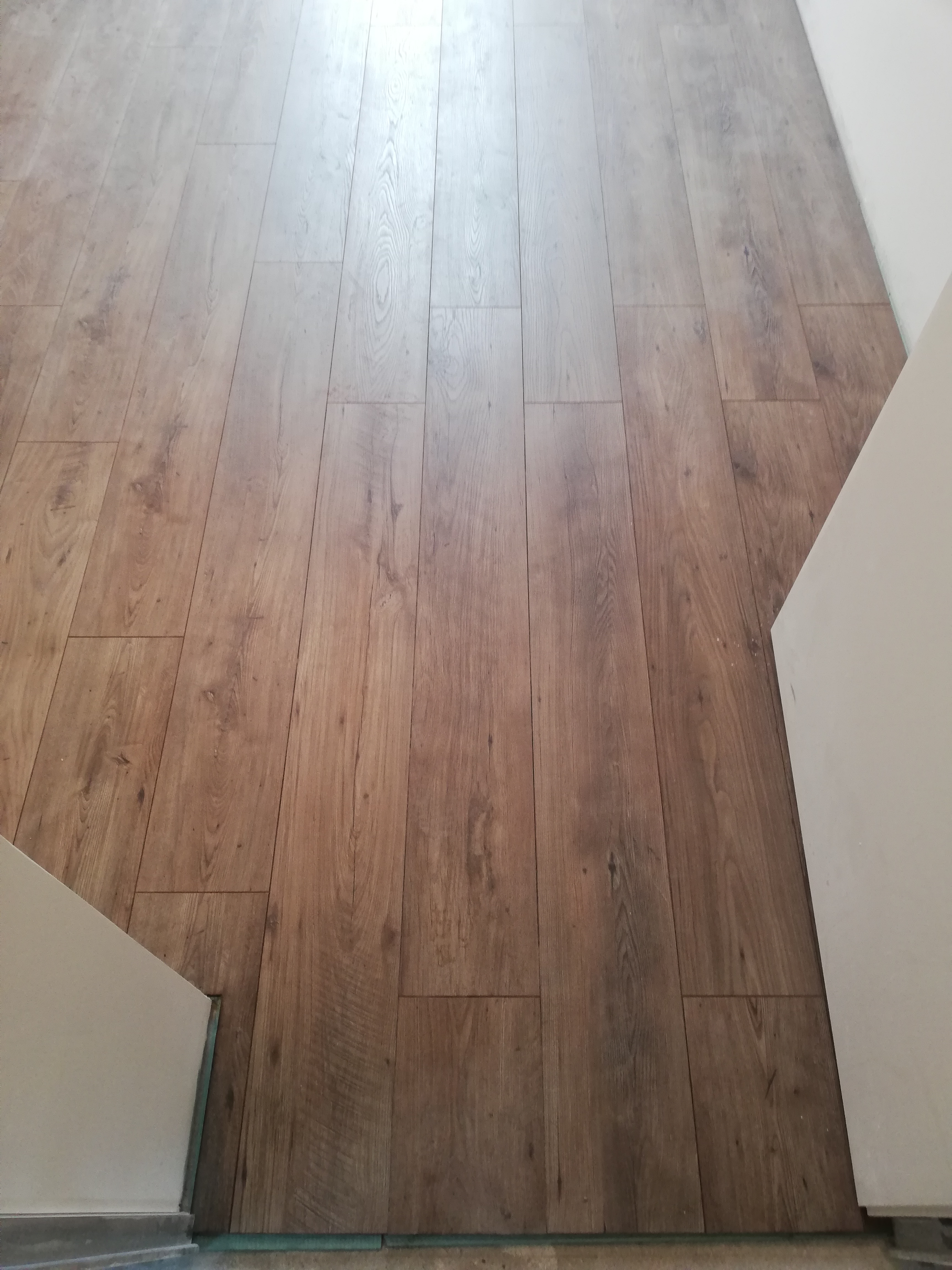 Ułożone panele podłogowe w odcieniach brązu, widoczne przy krawędziach ściany, z lekkim gradientem oświetlenia.