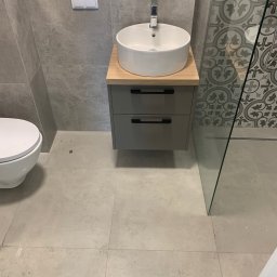 Euro Expo - Nowoczesna łazienka z umywalką nablatową na szafce z szufladami, obok toaleta i kabina prysznicowa z dekoracyjnymi płytkami na ścianie.