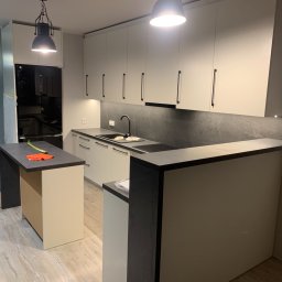 Euro Expo - Nowoczesna kuchnia z białymi szafkami, czarnymi uchwytami, szarym blatem i wyspą kuchenną z pomarańczowymi akcentami na blacie.