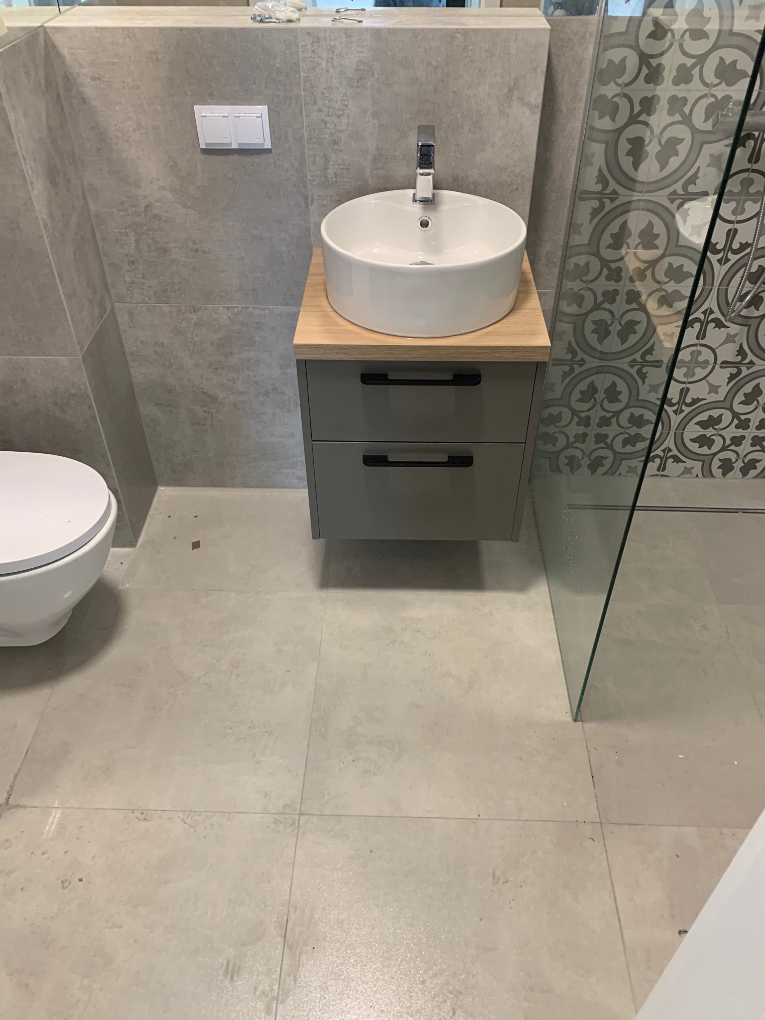 Nowoczesna łazienka z umywalką nablatową na szafce z szufladami, obok toaleta i kabina prysznicowa z dekoracyjnymi płytkami na ścianie.