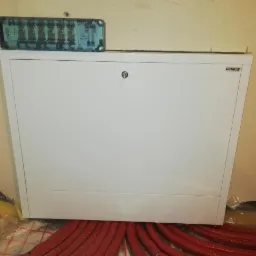 Rozdzielacz ogrzewania podłogowego marki Schilie z termostatami Salus, widoczne czerwone rury instalacji grzewczej na folii izolacyjnej.