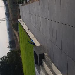 ABERBRUK - Nowoczesna nawierzchnia z dużych, ciemnoszarych płyt betonowych, przylegająca do trawnika z widoczną rurą nawadniającą i słupami wysokiego napięcia w oddali.