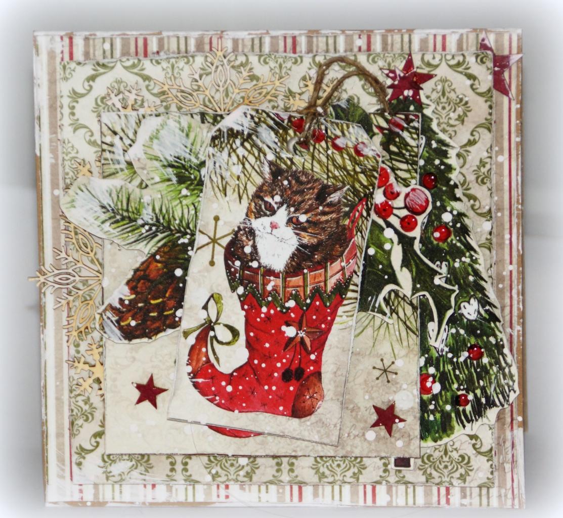 Ręcznie robiona kartka świąteczna z motywem kota w czerwonej skarpecie, choinki i dekoracyjnych płatków śniegu na wzorzystym tle.