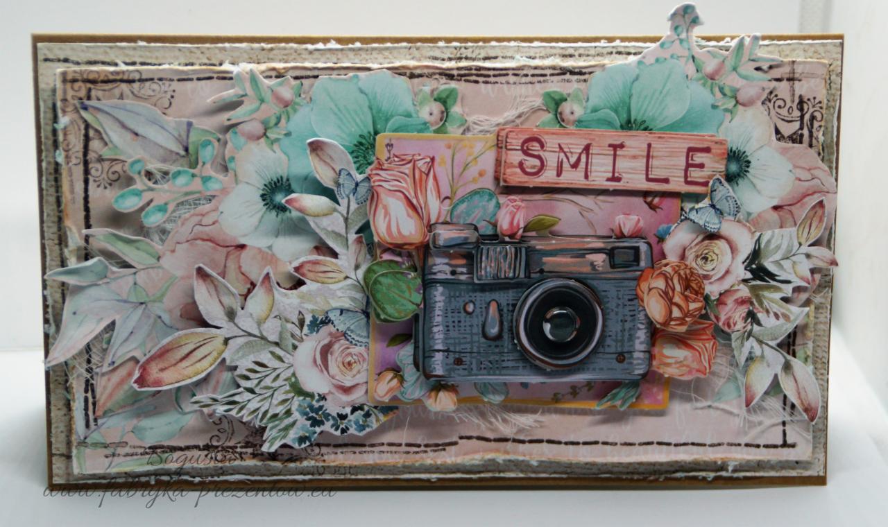 Ręcznie robiona kartka okolicznościowa z motywem kwiatowym, aparatem fotograficznym i napisem 'SMILE' na drewnianej deseczce, utrzymana w pastelowej kolorystyce.