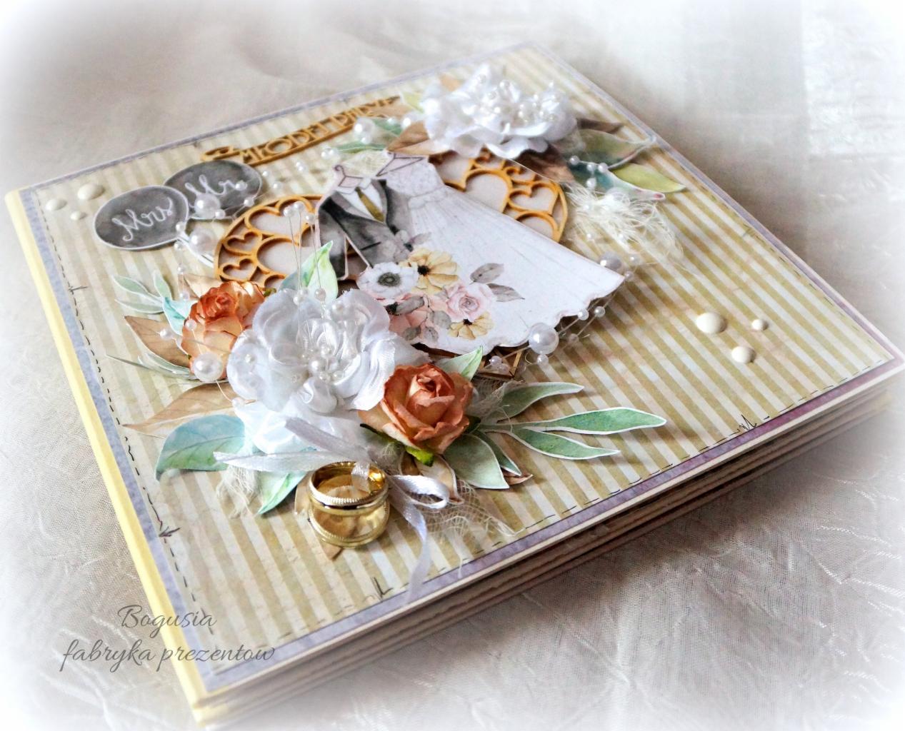 Ręcznie robiony album ślubny z dekoracjami kwiatowymi, obrączkami i motywem pary młodej na okładce.