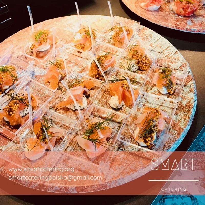 Elegancko podane przekąski z łososiem, sosem i koperkiem w przezroczystych naczyniach na drewnianej tacy.