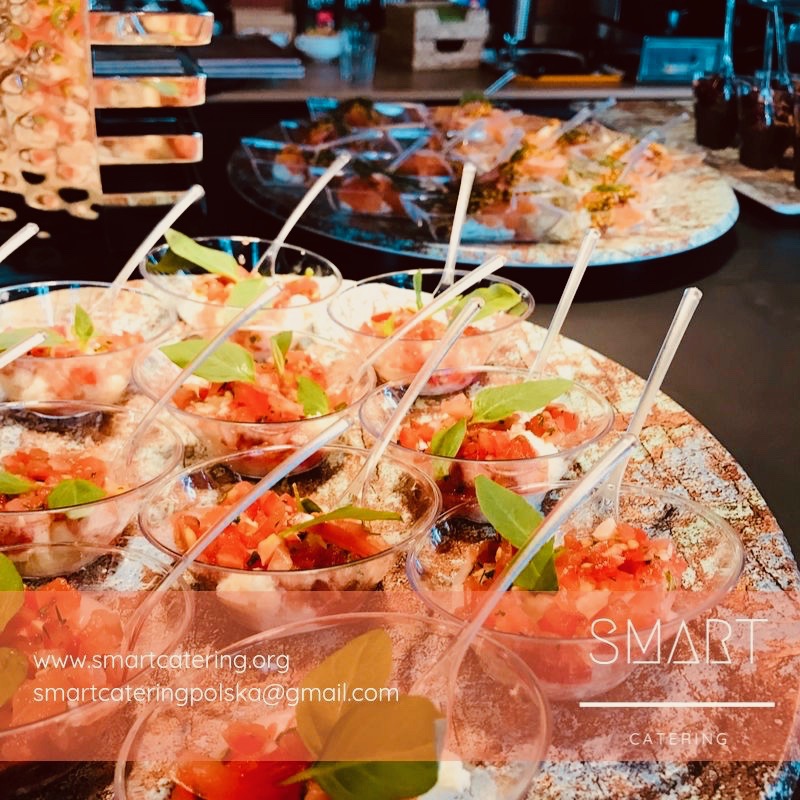 Szklane miseczki z sałatką pomidorową i bazylią, podane na marmurowej tacy cateringowej, z widocznym logo firmy Smart Catering w prawym dolnym rogu.