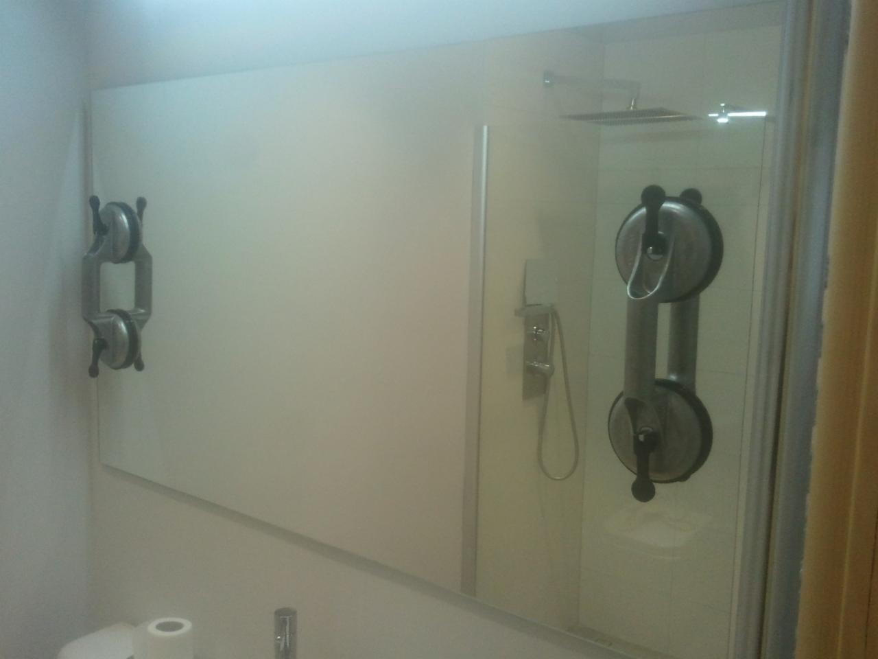 Montaż kabiny prysznicowej z użyciem przyssawek do szkła; widoczna kabina prysznicowa z zamontowanym panelem szklanym, przymocowanym do ściany za pomocą dwóch przyssawek. Po lewej stronie ściany...