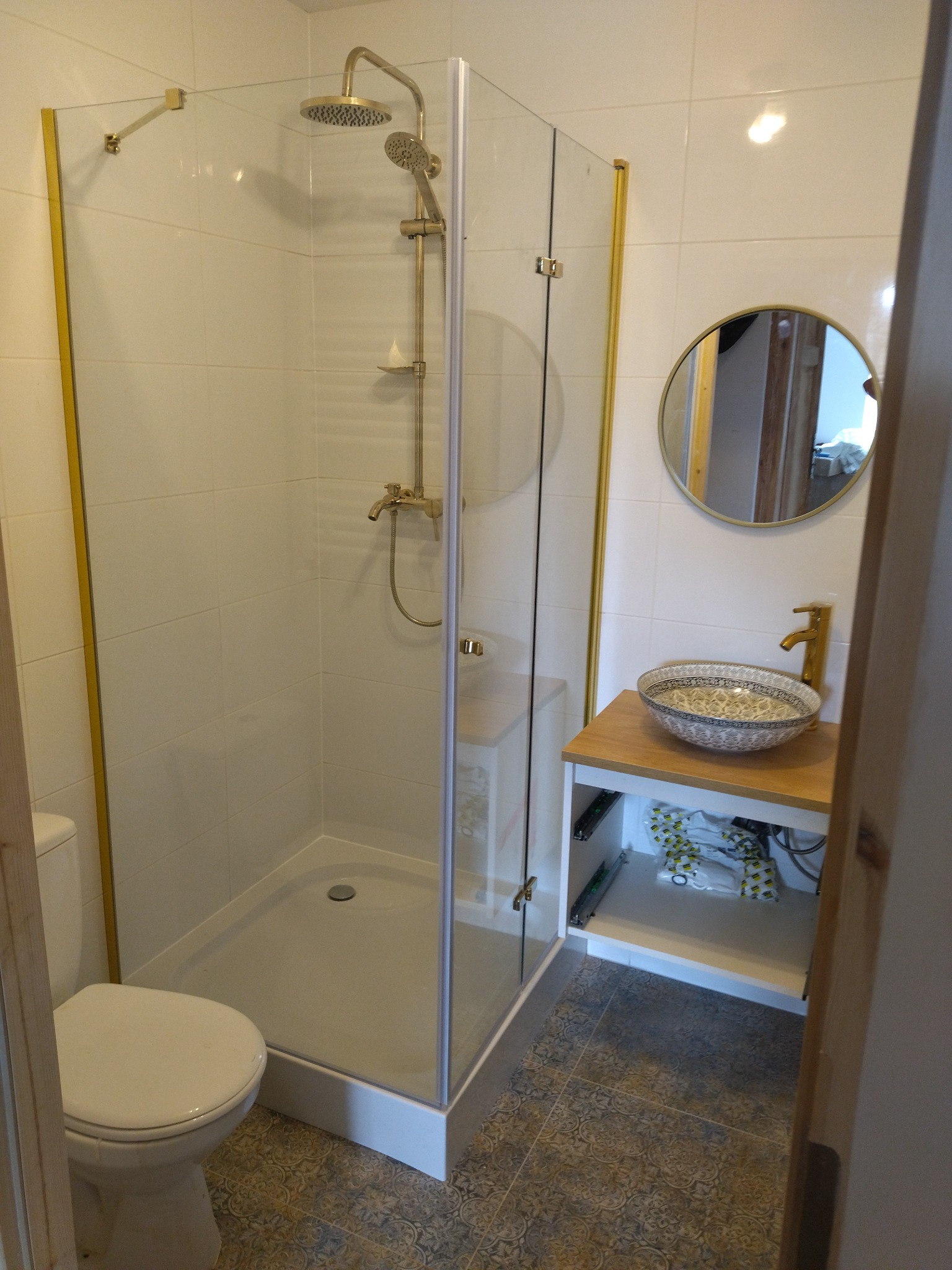 Wykończona łazienka w Lublinie z kabiną prysznicową ze złotymi ramami, okrągłym lustrem i umywalką nablatową o wzorzystym designie.