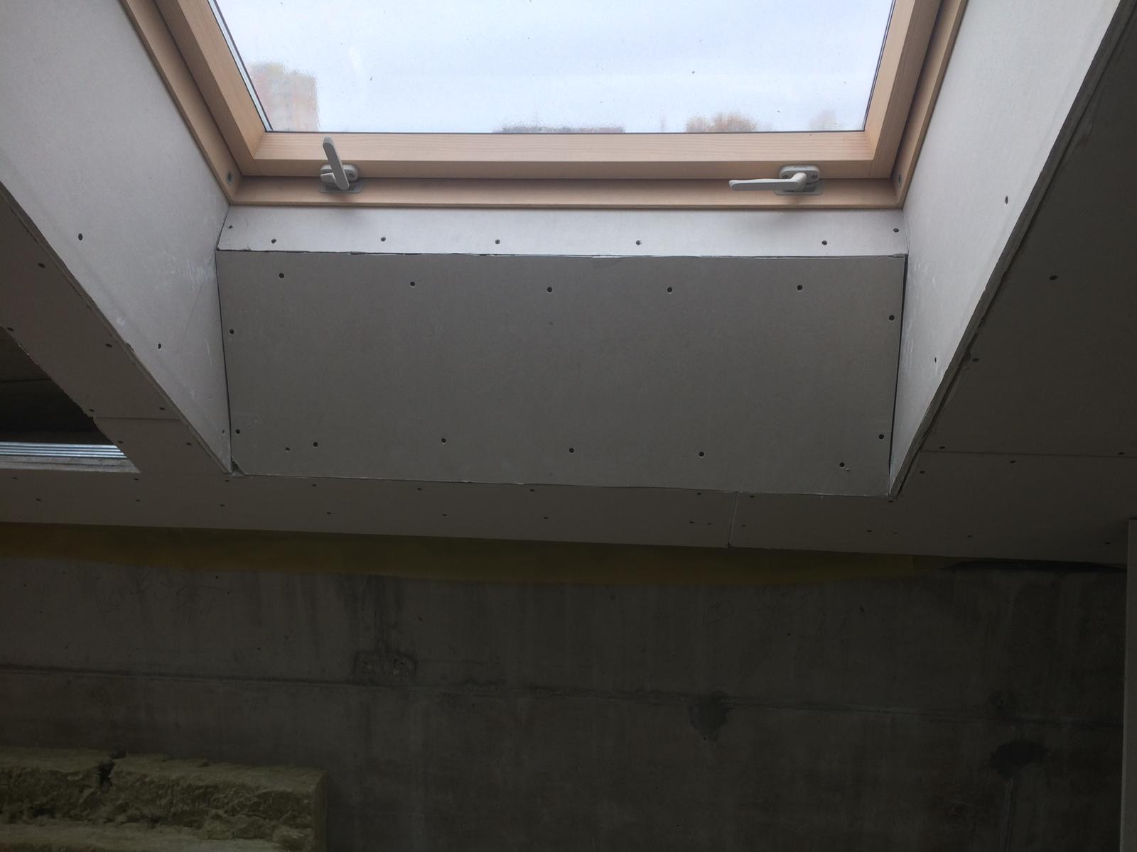 Montaż szarej płyty przy oknie dachowym, widoczne wkręty, surowe wykończenie, izolacja z wełny mineralnej w tle.