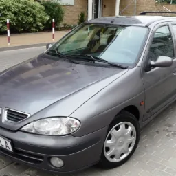 Szary samochód Renault Megane kombi z 2000 roku, zaparkowany na chodniku z kostki brukowej, widok z przodu i z boku.