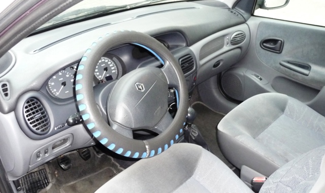 Wnętrze Renault Megane 2000 z szarą tapicerką i pokrowcem na kierownicy w kolorze czarnym z niebieskimi akcentami.