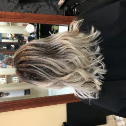 Włosy po koloryzacji z ciemnymi odrostami i blond refleksami, widoczne w lustrze salonu.