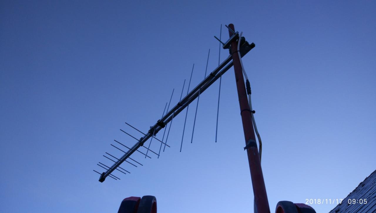 Antena Yagi-Uda na dachu domu, widoczna na tle błękitnego nieba o zmierzchu. Charakterystyczne elementy anteny i mocowanie do masztu. Widok z dołu.