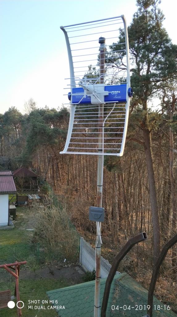 Antena telewizyjna zamontowana na maszcie w Sulęczynie, widok z góry na okoliczne drzewa i zabudowania, w tle las.
