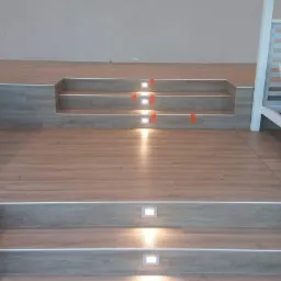 Wykończone wnętrze z drewnopodobną podłogą i schodami z wbudowanym oświetleniem LED, widoczne fragmenty białych łóżek piętrowych.