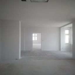 Józef Jastrzębki - Wnętrze w stanie deweloperskim, świeżo po gładziowaniu, z widocznymi oknami i surową podłogą, przygotowane do dalszych prac wykończeniowych.