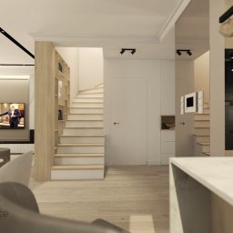 Studio Dobre Miejsce Sylwia Malewicz - Jasne wnętrze domu z drewnianymi schodami i elementami wyposażenia, w tle telewizor. Nowoczesny design, oświetlenie punktowe i minimalistyczny styl.