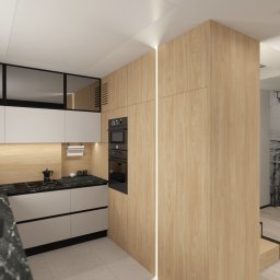 Studio Dobre Miejsce Sylwia Malewicz - Nowoczesna kuchnia z drewnianymi frontami, czarnym blatem i oknem z roletami. Widoczny fragment salonu z dekoracyjną tapetą. Minimalistyczny design.