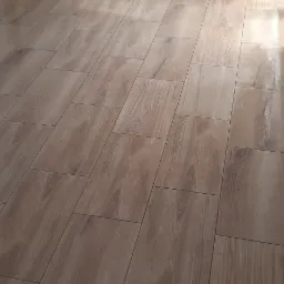 Ułożona, błyszcząca podłoga z płytek imitujących drewno, widoczne fragmenty białej zabudowy kuchennej i grzejnika.