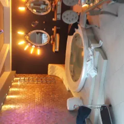 Luksusowa łazienka z okrągłą wanną z hydromasażem, dekoracyjną ścianą w odcieniach złota i różu, podświetlanymi lustrami w ozdobnych ramach oraz białymi płytkami podłogowymi.