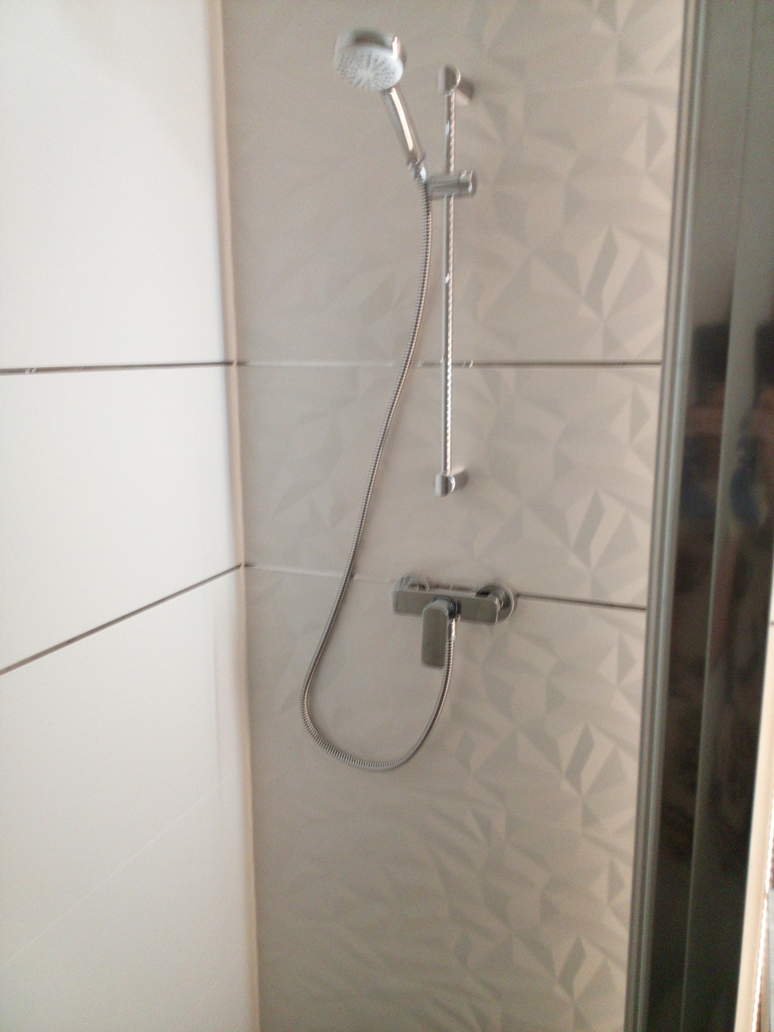 Kabina prysznicowa z chromowaną armaturą i geometrycznymi płytkami w odcieniach bieli i szarości.