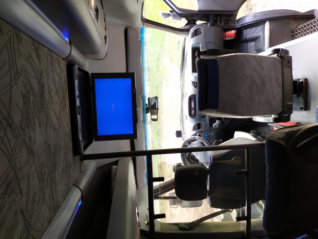 Wnętrze busa pasażerskiego z zamontowanym telewizorem i regulowanymi fotelami.