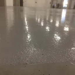 Świeżo wylana, błyszcząca, jasnoszara posadzka w hali przemysłowej, widoczne refleksy światła i delikatna struktura powierzchni.