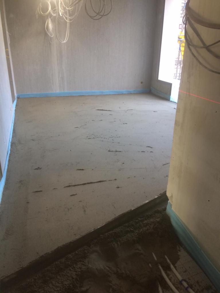 Wylewanie jastrychu w pomieszczeniu z widocznymi przewodami ogrzewania podłogowego i niebieską folią izolacyjną przy ścianach.