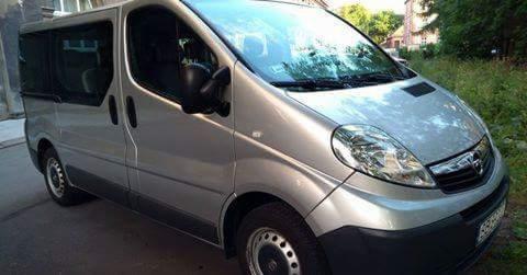 Srebrny Opel Vivaro z przyciemnianymi szybami zaparkowany na ulicy, widok z przodu z lekkiego ukosa.