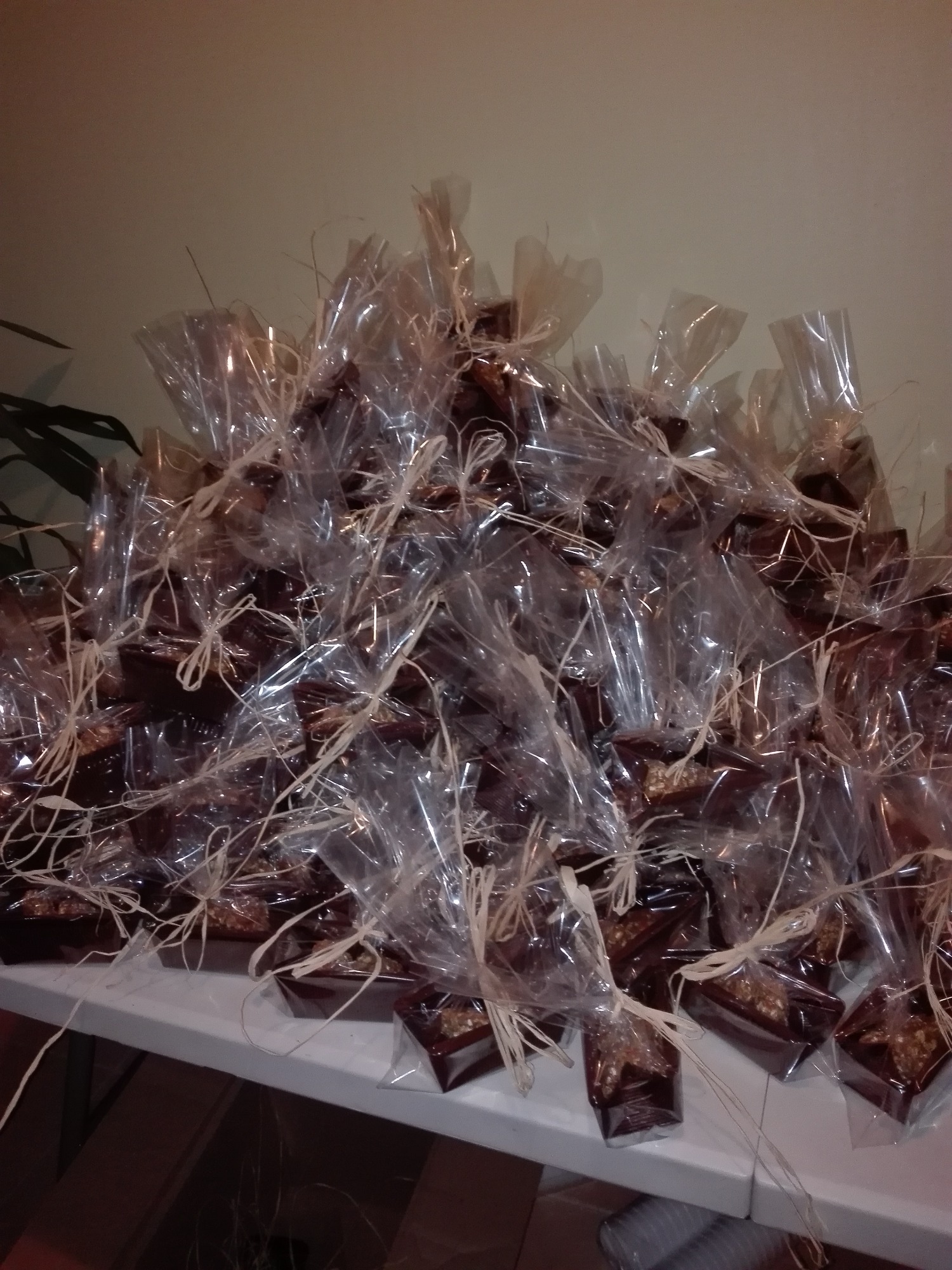 Stosik pojedynczo zapakowanych, brązowych, prostokątnych ciasteczek z orzechami, owiniętych w przezroczysty celofan i przewiązanych rafią, ułożonych na białym stole.