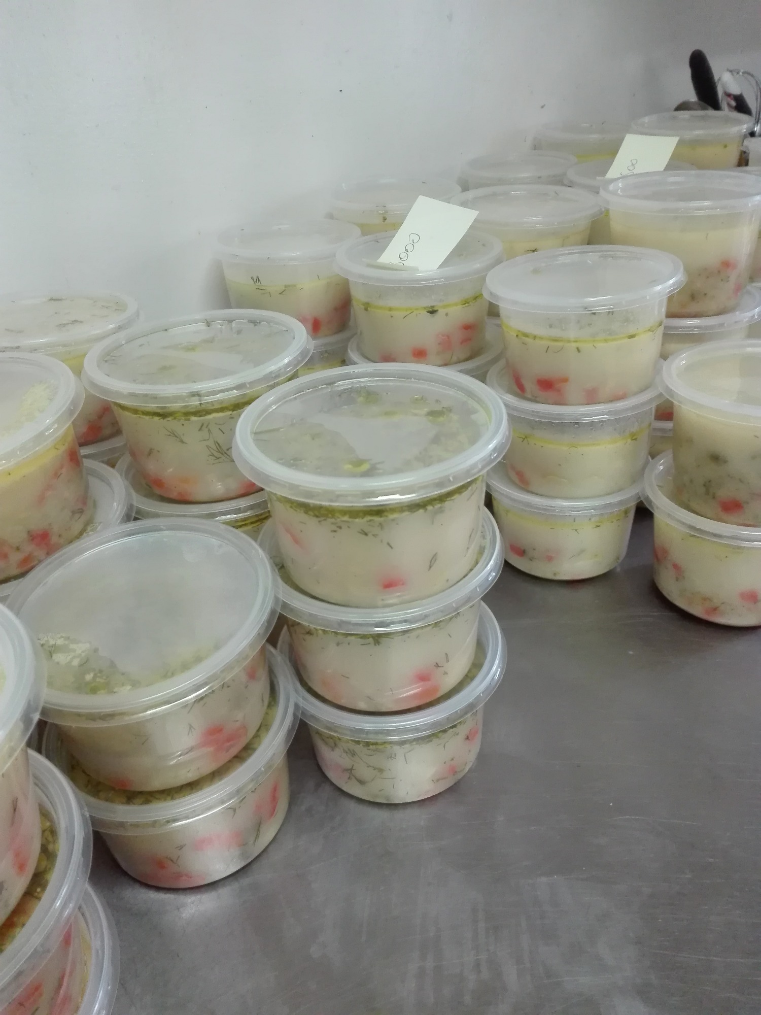 Porcje zupy krem w plastikowych pojemnikach, przygotowane do transportu, z etykietami na niektórych wieczkach.