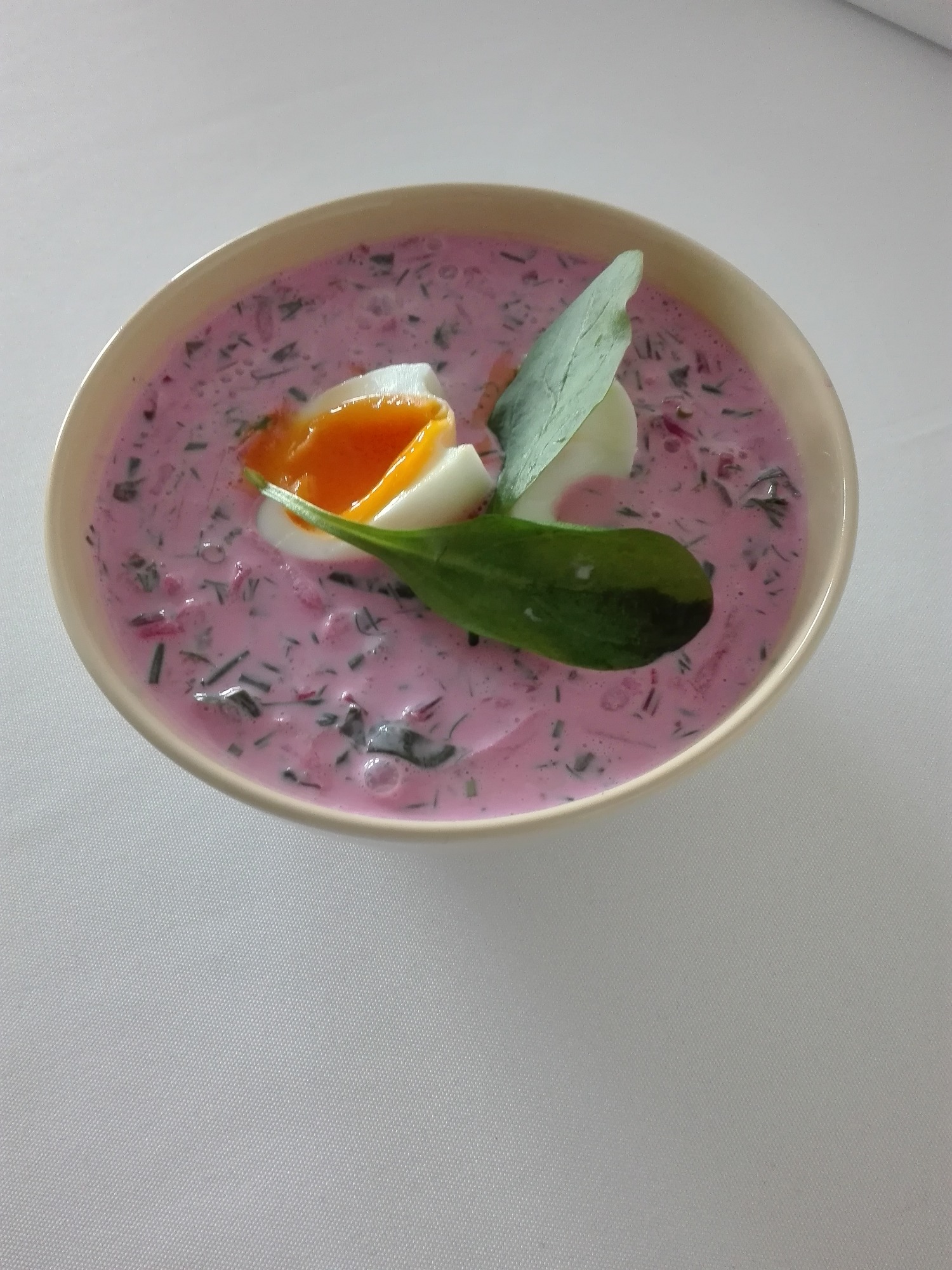 Chłodnik litewski z jajkiem na miękko i świeżymi ziołami, serwowany w miseczce w Warszawie.