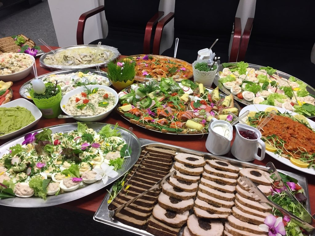 Bogato zastawiony stół różnorodnymi potrawami: sałatki, jajka faszerowane, pieczone mięso w plastrach, śledzie, pasty i dekoracje świąteczne, tworzące bufet.