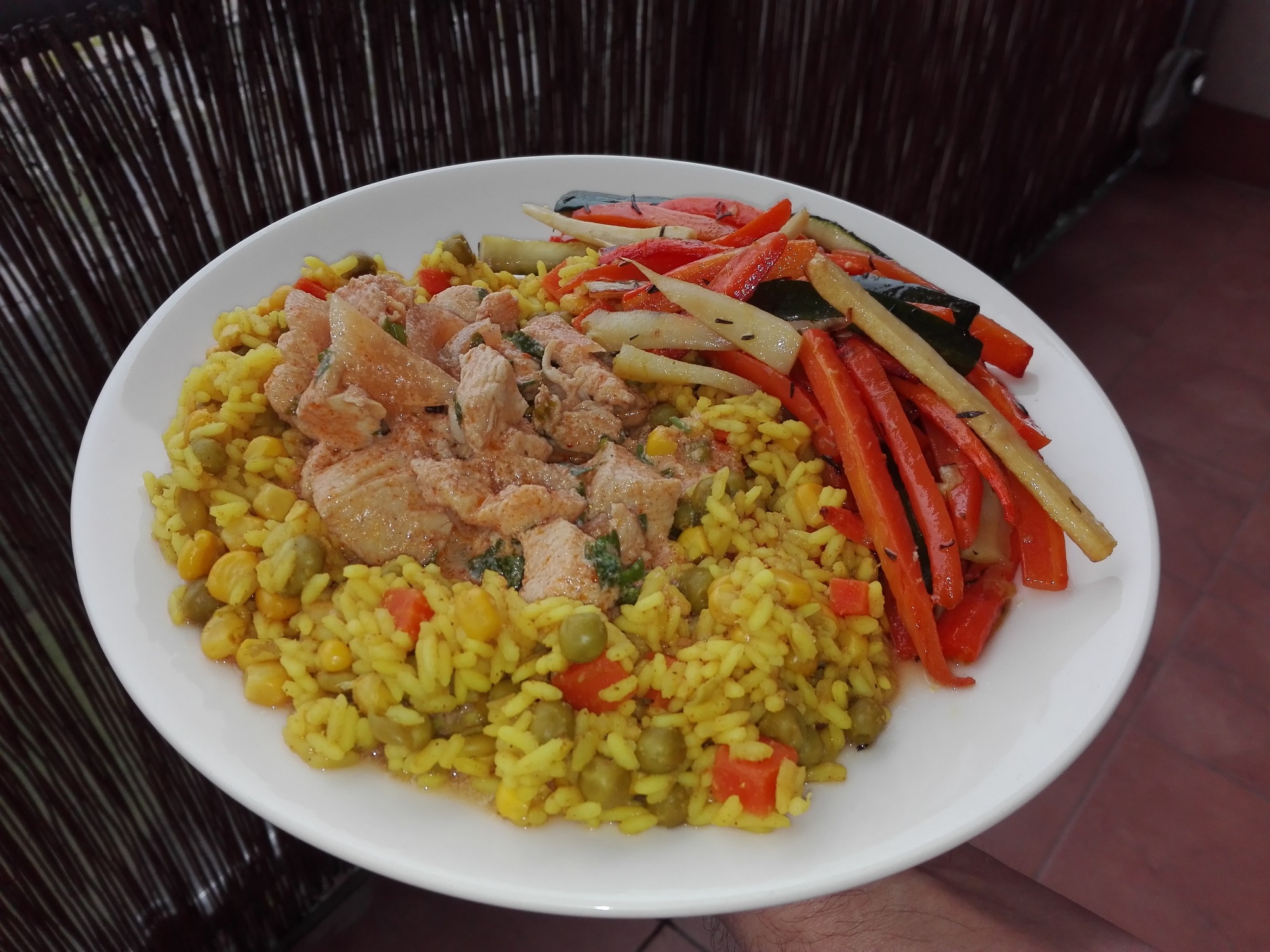 Porcja ryżu z warzywami i kurczakiem w sosie na białym talerzu z dekoracyjnym tłem.