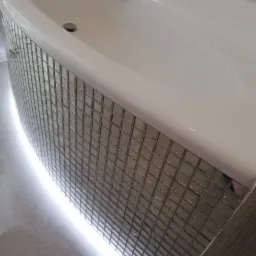 Obudowa wanny wykończona mozaiką w odcieniach szarości, z subtelnym podświetleniem LED u dołu.