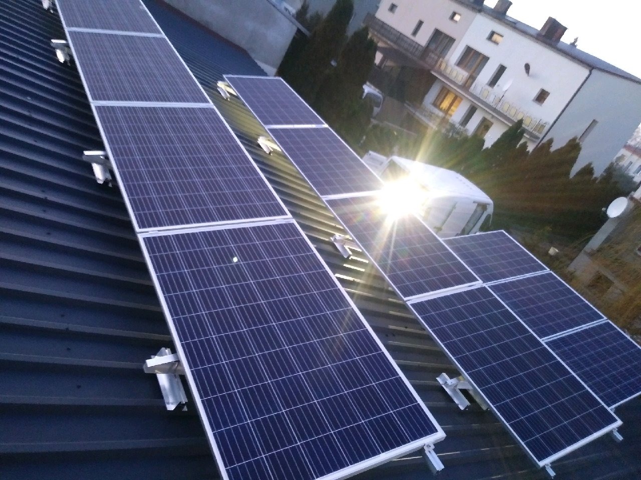 Rząd paneli słonecznych na metalowym dachu domu jednorodzinnego, widok z góry, blask słońca odbija się od powierzchni paneli.