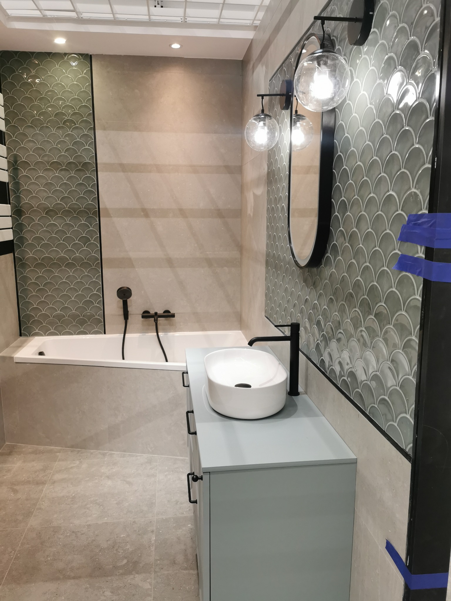 Nowoczesna łazienka z wanną, umywalką na szafce i płytkami w kształcie rybiej łuski. Oświetlenie punktowe i lustro kuliste dopełniają minimalistyczny design.