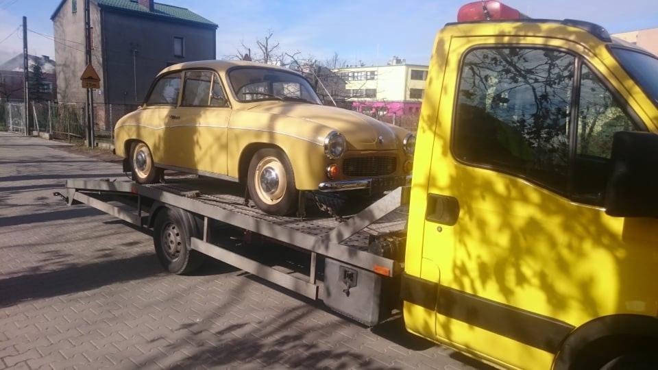 Żółty, zabytkowy samochód Warszawa M20 na platformie lawety holowniczej w słoneczny dzień.