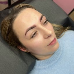 Ewa Zyzańska permanent make-up - Kobieta leżąca na poduszce z widocznymi brwiami po zabiegu microbladingu, delikatny makijaż permanentny brwi, jasna cera, błękitny sweter.