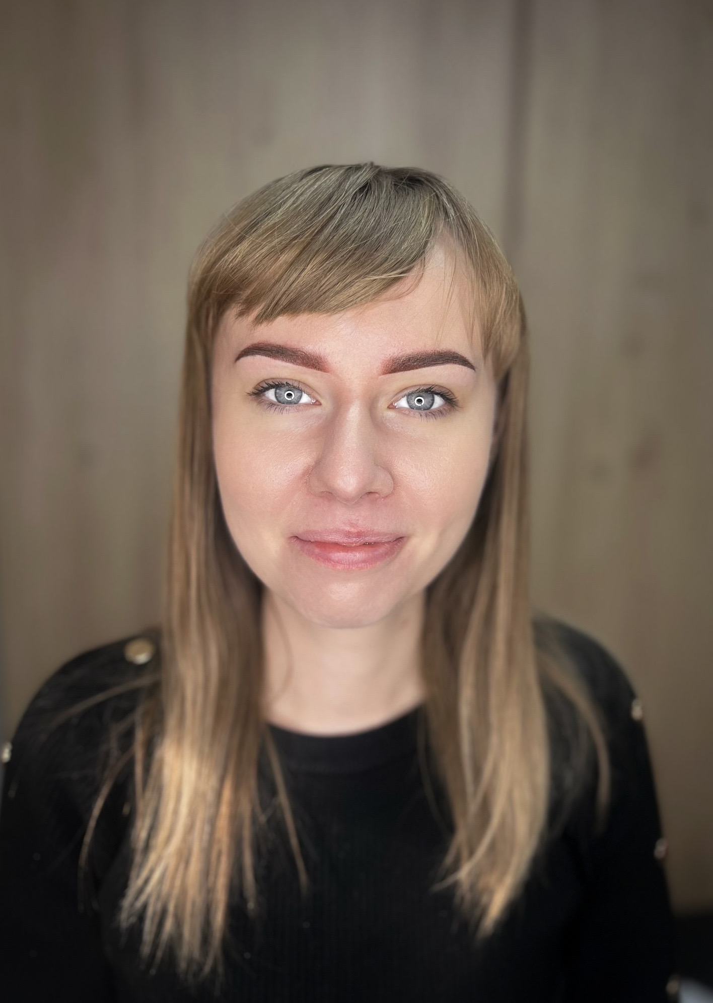 Portret kobiety z jasnymi włosami i świeżo wystylizowanymi brwiami, z delikatnym uśmiechem i niebieskimi oczami.