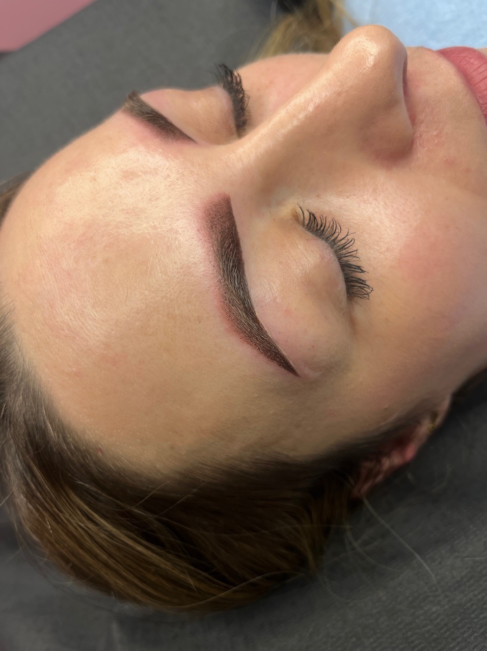 Kobieta po zabiegu makijażu permanentnego brwi metodą pudrową, widoczne świeżo wykonane, ciemne brwi z delikatnym cieniowaniem, ujęcie z góry.