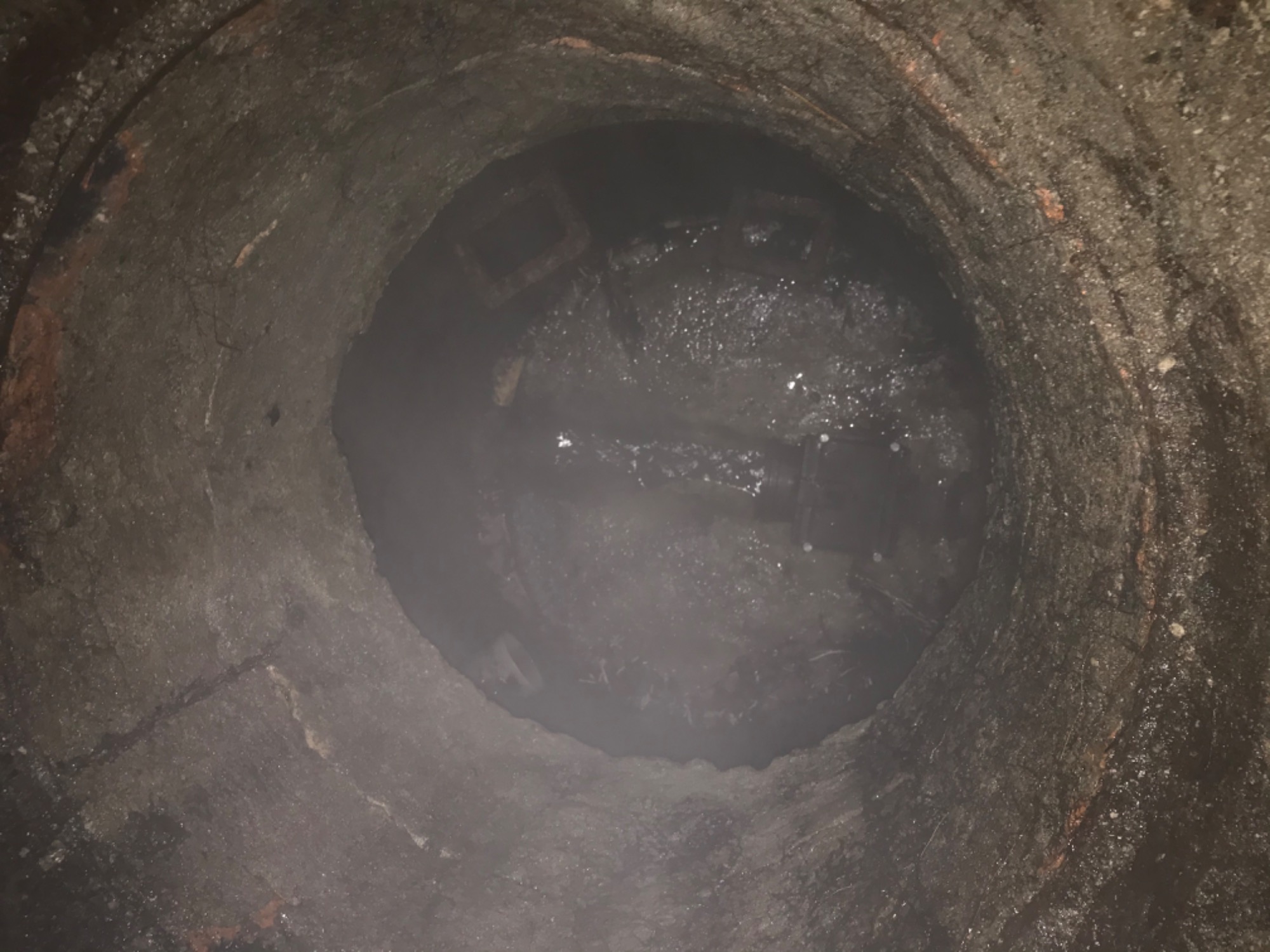 Wnętrze betonowej studzienki kanalizacyjnej wypełnionej wodą, widoczne elementy instalacji.