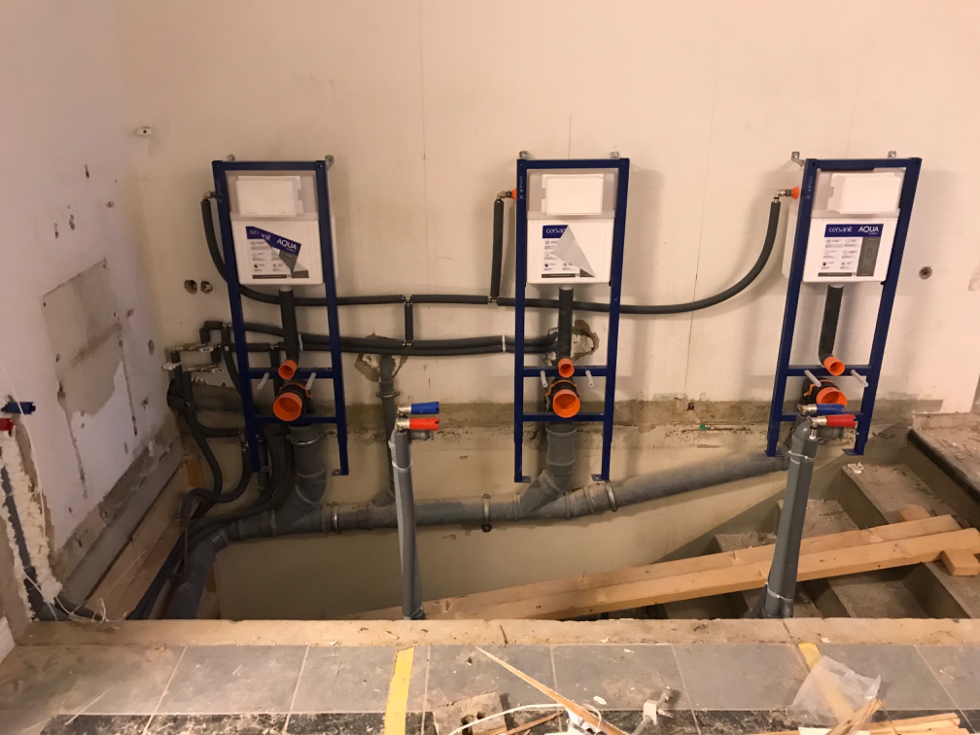 Trzy stelaże podtynkowe do WC zamontowane w łazience w trakcie prac instalacyjnych, widoczne rury kanalizacyjne i wodne, ściany przygotowane do dalszych prac wykończeniowych.