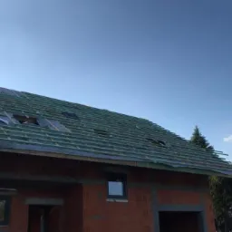 Wymiana dachu w trakcie: widoczne krokwie, membrana dachowa i komin na tle błękitnego nieba.